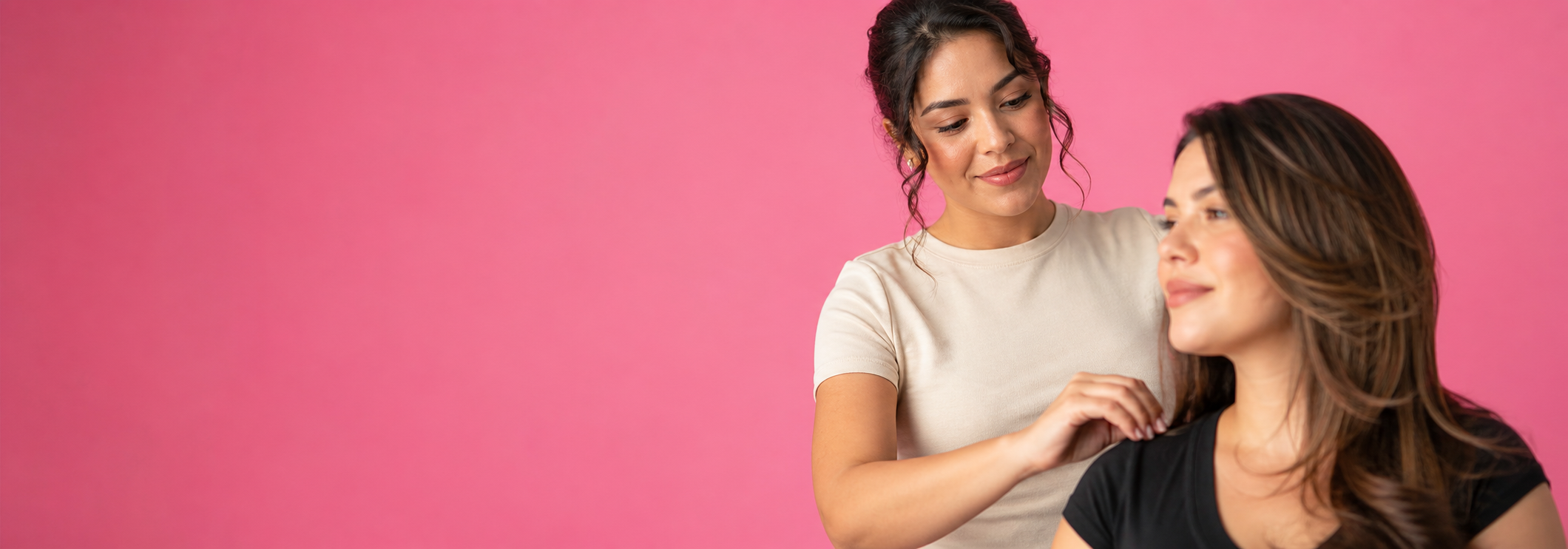 Hair stylist styling a smiling client, against a pink backdrop